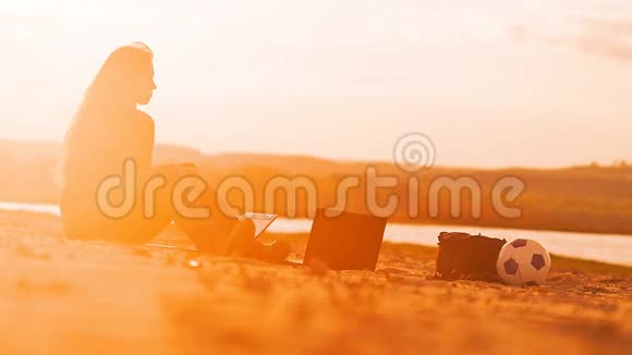 坐在沙滩上的女孩拿着笔记本电脑视频的预览图