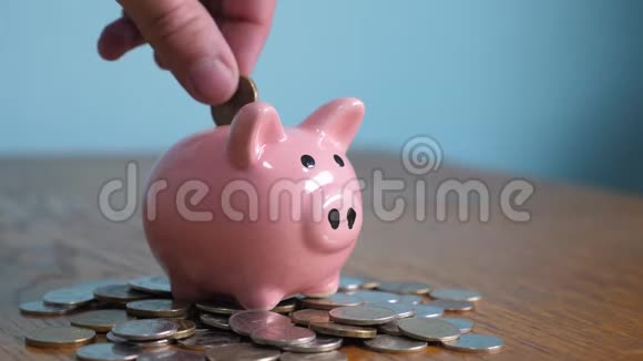 猪银行业务站在一堆硬币的概念上一只手把硬币放在生活方式的储蓄罐里视频的预览图