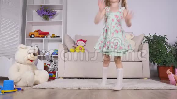 快乐的金发女孩穿着裙子在家里或幼儿园的一间阳光明媚的白色房间里在室内尽情跳舞视频的预览图