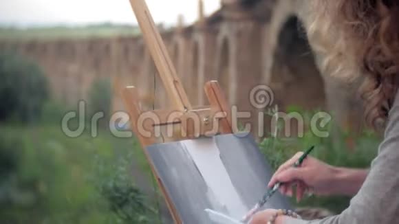 年轻女子在画架上画画刷旧旧桥视频的预览图