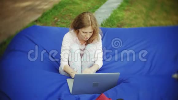 年轻女子用手提电脑躺在公园的一个休息区软泡芙上视频的预览图