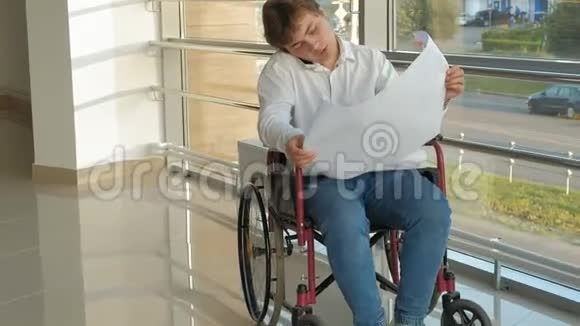 一位坐在轮椅上的残疾商人在窗户上画着一张大纸通过电话讨论工作视频的预览图