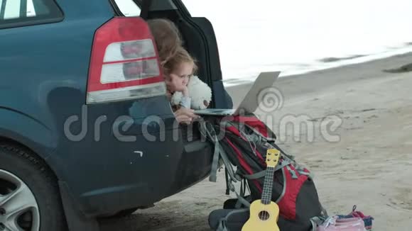 美丽的年轻女子和她的小女儿正坐在海边的一辆敞篷汽车的后备箱里视频的预览图