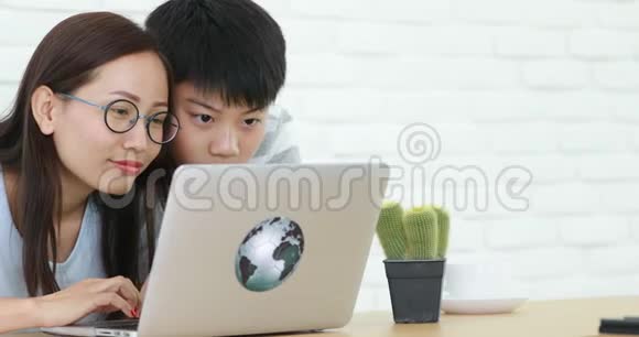 快乐的亚洲家庭母亲和儿子一边看着电脑笔记本一边笑视频的预览图
