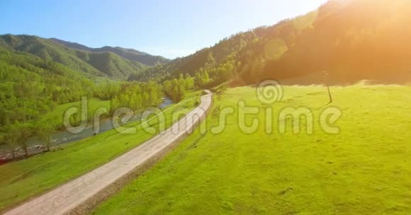 空中UHD4K视野阳光明媚的夏日清晨低空飞越高山乡村土路和草地视频的预览图