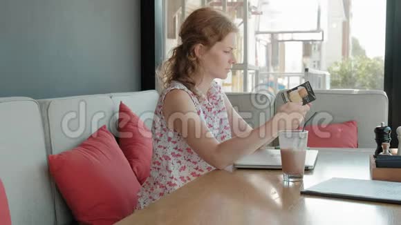 年轻的女商人坐在餐馆的一张桌子旁她带着一台可以上网的笔记本电脑它可以检查视频的预览图