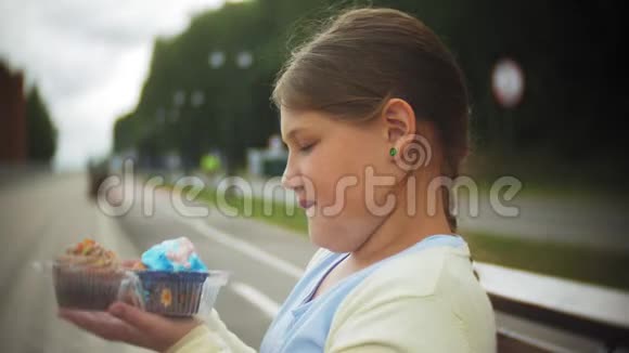靠近可爱的小胖女孩双手坐在公园的长凳上吃蛋糕视频的预览图