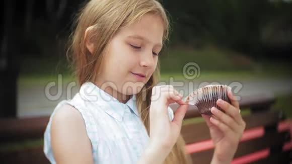 靠近可爱的小女孩吃蛋糕双手坐在公园的长凳上视频的预览图