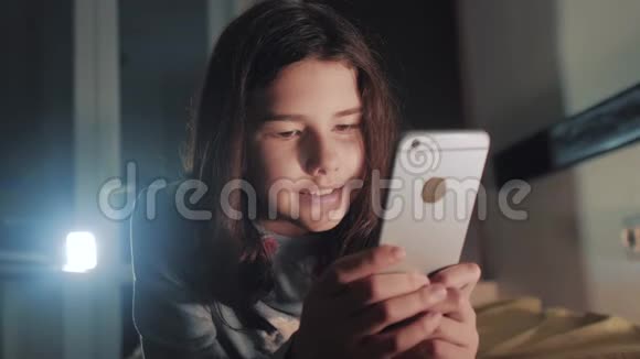 十几岁的女孩网上购物在她的智能手机上看起来生活方式在床上过夜一个小少女写的视频的预览图