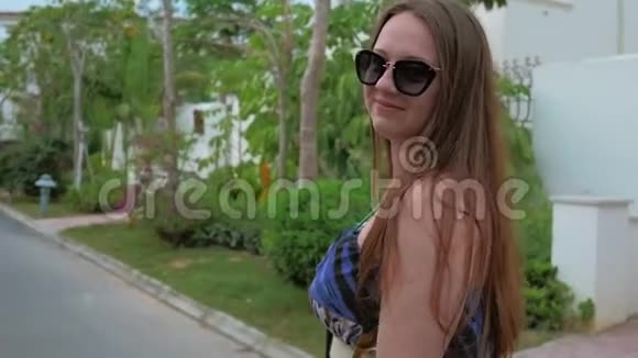 一个穿着蓝色连衣裙的年轻女孩正沿着热带城市的街道行走中弹视频的预览图