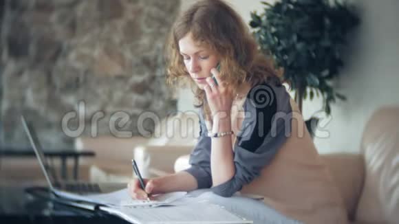 年轻漂亮的女商人坐在沙发上桌上放着平板电脑看着报纸视频的预览图