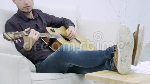 坐在沙发上弹吉他的年轻人视频的预览图