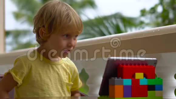 热带地区的男孩用平板电脑和无线耳机通过视频通话与朋友和家人交谈视频的预览图