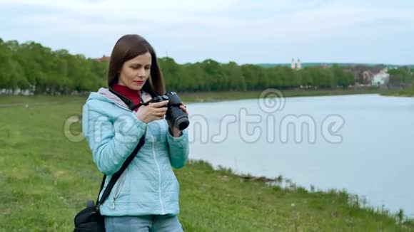 美丽的女孩游客在河岸上用专业的照相机拍照视频的预览图