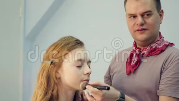 一个男性化妆师给一个年轻的女人化妆主人讲述一群女孩的化妆硕士班视频的预览图