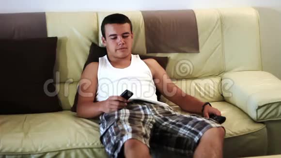 年轻迷人的少年在沙发上看电视视频的预览图
