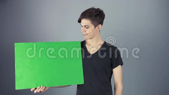 微笑穿着黑色衬衫的年轻人拿着绿色钥匙片海报灰色背景视频的预览图