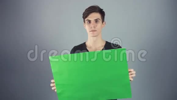 微笑穿着黑色衬衫的年轻人拿着绿色钥匙片海报灰色背景视频的预览图