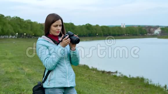美丽的女孩游客在河岸上用专业的照相机拍照视频的预览图