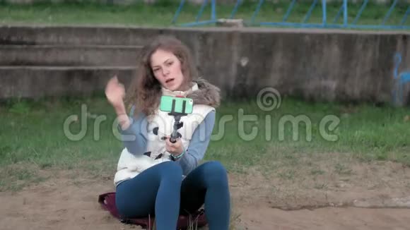 漂亮女孩微笑着用智能手机在公园里自拍视频的预览图