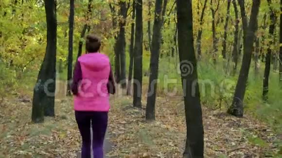 跑步女子跑步者在秋天的森林小径上慢跑适合女性运动健身模特运动员跑步训练视频的预览图