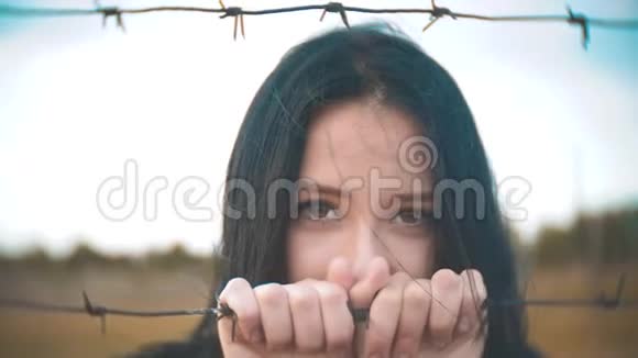 女孩黑发难民背后铁丝网营地慢动作视频自由的概念令人不安女人的手和铁丝网视频的预览图