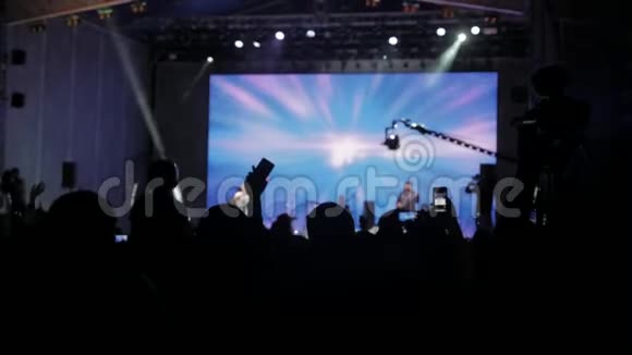 音乐音乐会上的人群在明亮多彩的舞台灯光前成群的观众在智能手机上拍照视频的预览图