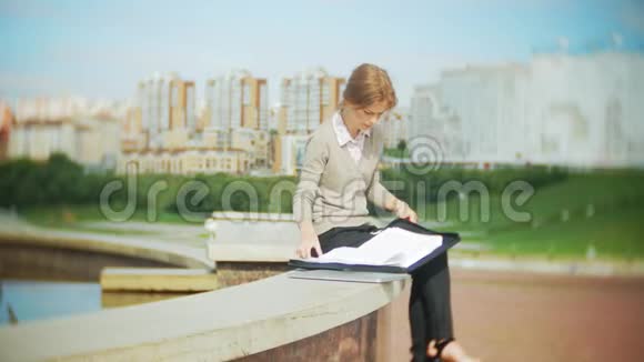 年轻的商务女性坐在台阶上手提电脑在商务中心阅读文件视频的预览图