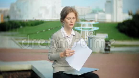 年轻的商务女性坐在台阶上手提电脑在商务中心阅读文件视频的预览图