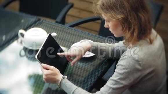 年轻女子用平板电脑和电话在咖啡馆喝茶视频的预览图