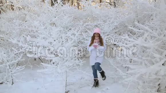穿着粉红色帽子和手套的漂亮女孩在冬天的雪林里视频的预览图