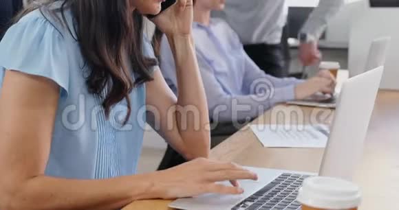 女性高管在使用笔记本电脑时使用手机视频的预览图