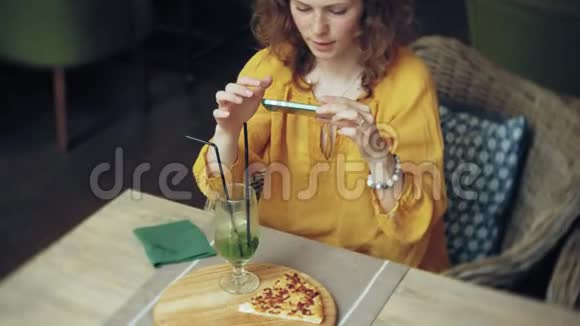 年轻女子在智能手机的咖啡馆里吃馅饼视频的预览图