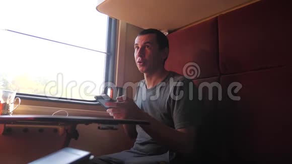 男人坐在火车车厢上手里拿着智能手机喝着咖啡生活方式和茶慢动作视频的预览图