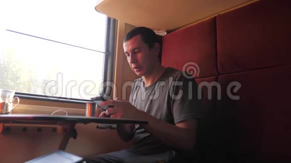 男人坐在火车车厢里拿着智能手机喝着咖啡和茶慢动作视频男人视频的预览图