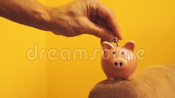 猪银行的经营理念一只手是把硬币放在黄色背景上的储蓄罐里的生活方式省钱就是视频的预览图