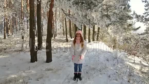 穿着粉红色帽子和手套的漂亮女孩在冬天的雪林里视频的预览图