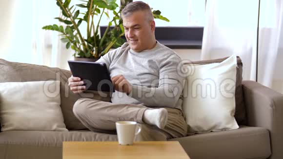 有平板电脑的男人坐在家里的沙发上视频的预览图