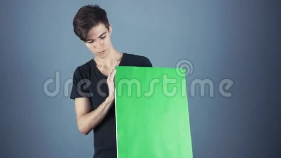 身穿黑色衬衫手持绿色钥匙单的年轻人海报灰色背景视频的预览图