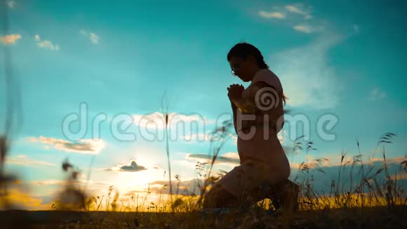 女孩在日落时双手交叉祈祷剪影慢动作视频女孩双手交叉祈祷祈求上帝视频的预览图