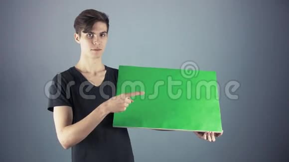 身穿黑色衬衫手持绿色钥匙单的年轻人海报灰色背景视频的预览图