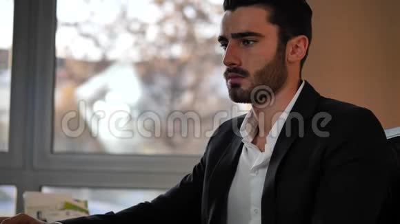 一位英俊的年轻商人坐在办公桌前视频的预览图
