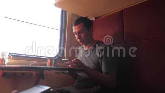 男人坐在火车车厢里手里拿着智能手机喝着咖啡和茶慢动作视频的预览图