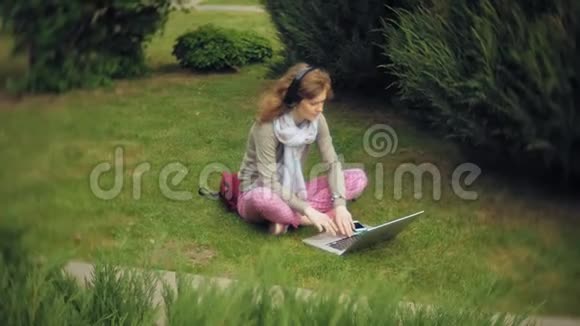 有笔记本电脑的女人在美丽的绿色公园的草坪草地上放松一个常年在植物园里工作的年轻女子视频的预览图