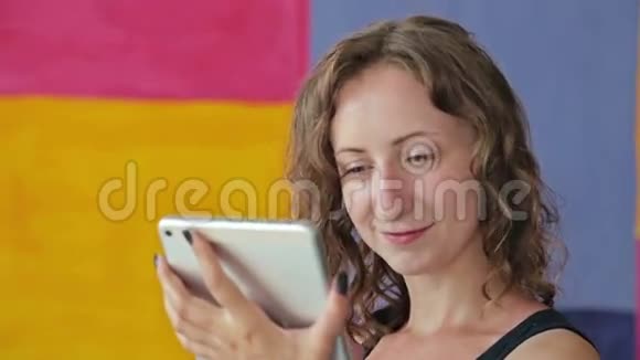 年轻的卷发妇女使用平板电脑视频的预览图