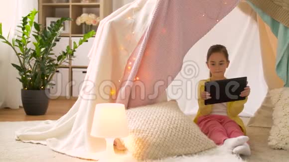 带平板电脑的小女孩在家里的儿童帐篷里视频的预览图