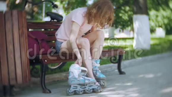 女人穿着溜冰鞋坐在公园的长凳上视频的预览图