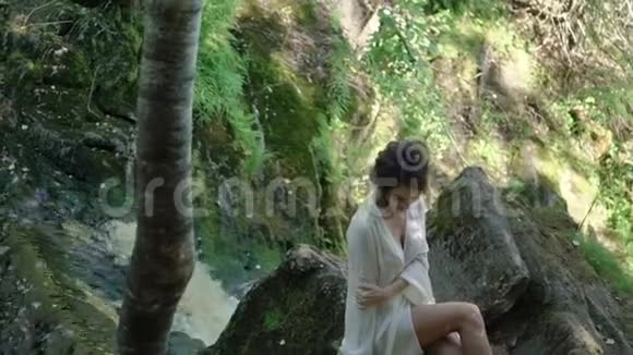 年轻女子坐在瀑布附近的岩石上视频的预览图