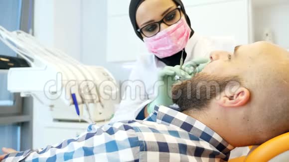 女牙医戴头巾检查病人牙齿的照片视频的预览图