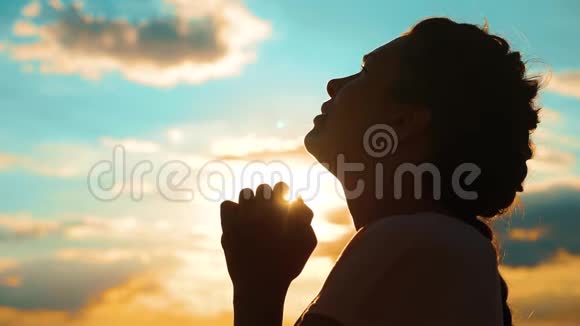 女孩在祈祷女孩在日落时交叉双手祈祷剪影慢动作视频生活方式女孩双手合拢视频的预览图